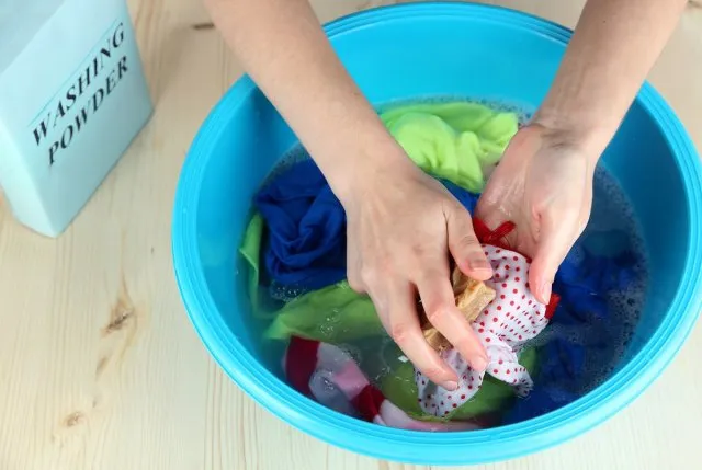 Hand washing in plastic bowl on wooden table close-up